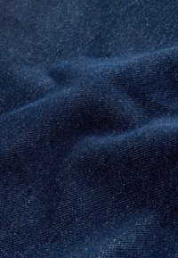Gros plan d’un tissu en jean bleu foncé montrant sa texture et son motif de tissage avec de légères rides et plis.