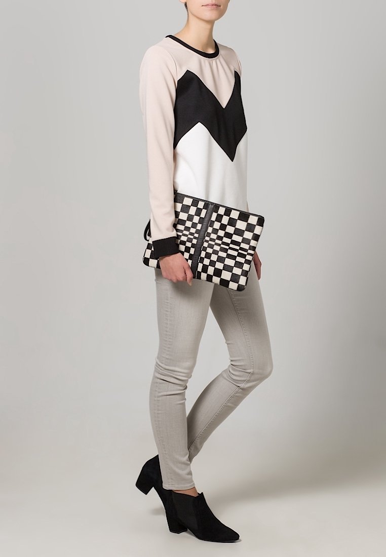 Svart- och vitrandig långärmad topp med chevronmönster, ljusgrå jeans, svarta ankelskålar och en rutigt clutchväska. Enkel, modern design.