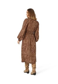 Rochie maxi cu imprimeu de zebra maro, cu mâneci lungi și talie strânsă; combinată cu cizme bej până la genunchi. Textură de material neted și ușor.