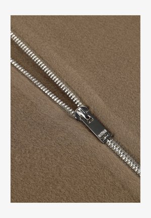 Silberner Metallreißverschluss teilweise geöffnet auf strukturiertem braunem Stoff, der ineinandergreifende Zähne und einen glatten Ziehgriff zeigt.