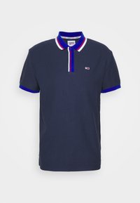 Polo bleu marine à manches courtes en tissu texturé. Il présente un col classique avec des accents rouges, blancs et bleus, ainsi qu'un petit logo sur la poitrine.