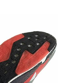 Semelle d'une chaussure de sport présentant une semelle en caoutchouc noire et rouge avec des motifs texturés pour l'adhérence et la durabilité.