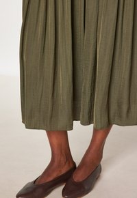 Gonna midi plissettata verde oliva con una texture fluida, abbinata a scarpe basse marrone scuro con design a punta rotonda.