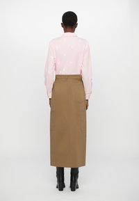 Camicia rosa a maniche lunghe con ricami floreali, abbinata a una gonna khaki a vita alta con due grandi tasche laterali e stivali neri al ginocchio.