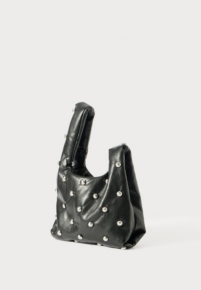 Bolsa de couro preta com duas alças curtas, apresentando um design acolchoado e tachas metálicas distribuídas de forma uniforme pela superfície.
