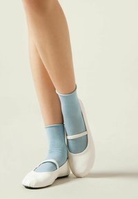 Bailarinas blancas con un diseño de punta redonda y una cinta contrastante, combinadas con calcetines tobilleros de color azul claro, hechos de un material brillante y texturizado.