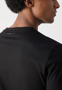Camiseta negra de manga corta, hecha de una suave tela de algodón, con un pequeño logo "MORATO" bordado en la parte posterior del cuello.