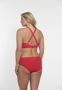 Červený bikinový set se zkříženým topem s nastavitelnými ramínky a odpovídajícími kalhotkami. Hladká textura s diskrétním logem na zadní straně.