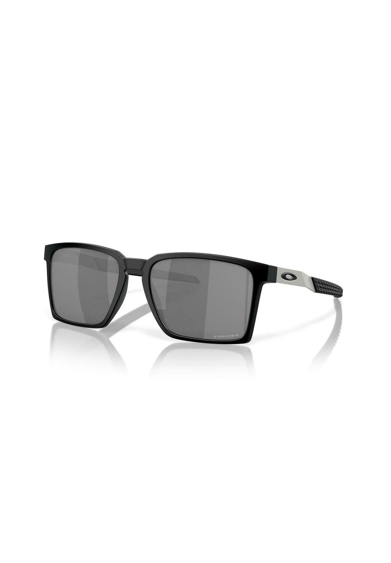 Occhiali da sole neri quadrati con lenti grigie, caratterizzati da un design elegante e da un accessorio laterale nero testurizzato. Montatura in plastica leggera.