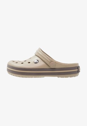 Sabots Crocs beige à enfiler avec des trous de ventilation, sangle arrière ajustable et rayures de semelle brun foncé.