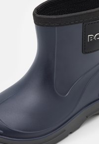 Gros plan sur une botte de pluie ankle imperméable bleu marine avec des bordures élastiques noires et une semelle en caoutchouc.