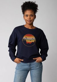 Marineblaues Sweatshirt mit einem runden Grafikdesign, das gelbe, orange und rote horizontale Streifen zeigt, die einen Sonnenuntergang und Silhouetten von Bäumen darstellen.