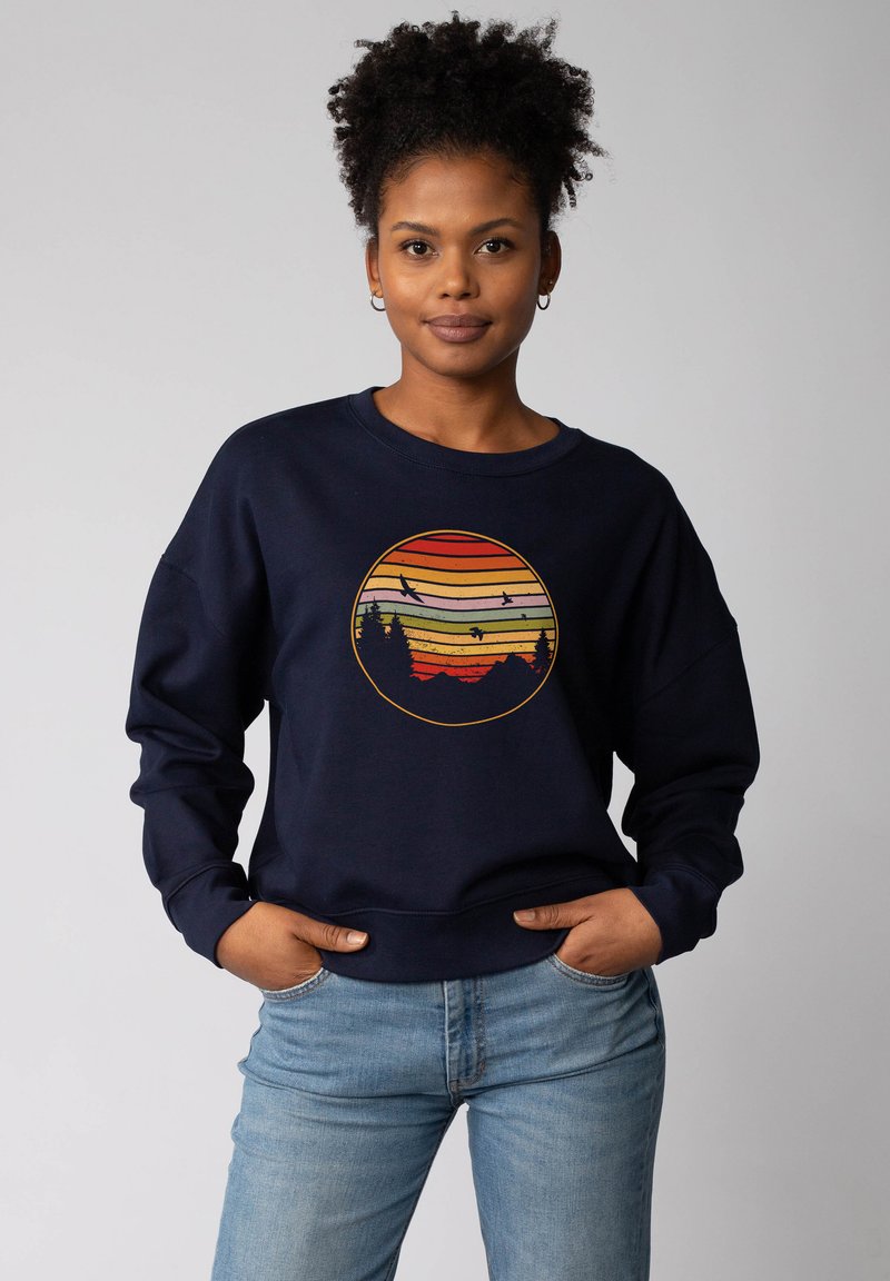Marineblaues Sweatshirt mit einem runden Grafikdesign, das gelbe, orange und rote horizontale Streifen zeigt, die einen Sonnenuntergang und Silhouetten von Bäumen darstellen.