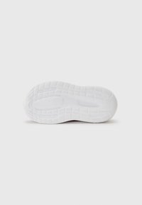 Semelle de chaussure de sport blanche avec un motif texturé, présentant des sections surélevées pour l'adhérence et une zone centrale lisse pour la flexibilité.