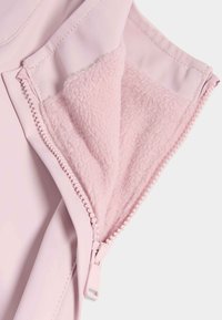 Gros plan sur la fermeture éclair d'une veste rose clair partiellement ouverte, révélant une doublure en polaire douce et texturée à l'intérieur.