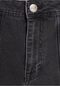 Los pantalones de mezclilla negra presentan un botón plateado con la inscripción "DEF" grabada, mostrando una textura de tela distintiva y costuras en contraste a lo largo de las costuras.