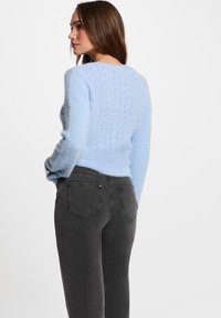 Suéter difuso de color azul claro con un patrón texturizado en forma de diamante en la parte posterior; combinado con jeans gris oscuro que tienen bolsillos traseros.