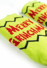 Calze verde giallastro brillanti con il testo rosso "BUON NATALE" e motivi a zigzag neri su uno sfondo bianco.