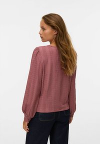 Blouse à manches longues, texturée, en rose poussiéreux avec des manches bouffantes froncées, un col rond et une coupe décontractée, associée à un jean en denim noir.