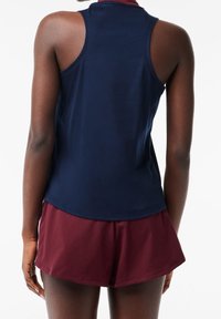 Marinblå ärmlös topp i mjukt tyg, kombinerad med vinröda shorts. Toppens design har en rund halsringning och en smal passform.