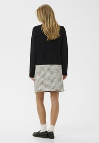 Črna pulover s sproščenim krojem, v kombinaciji s bež in črno karirasto krilo. Črne čevlje in bele nogavice dopolnjujejo obleko.