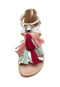 Sandalia blanca con tiras metálicas, suela plana y borlas decorativas en varios colores: rojo, rosa y verde. Textura suave, acentos trenzados.