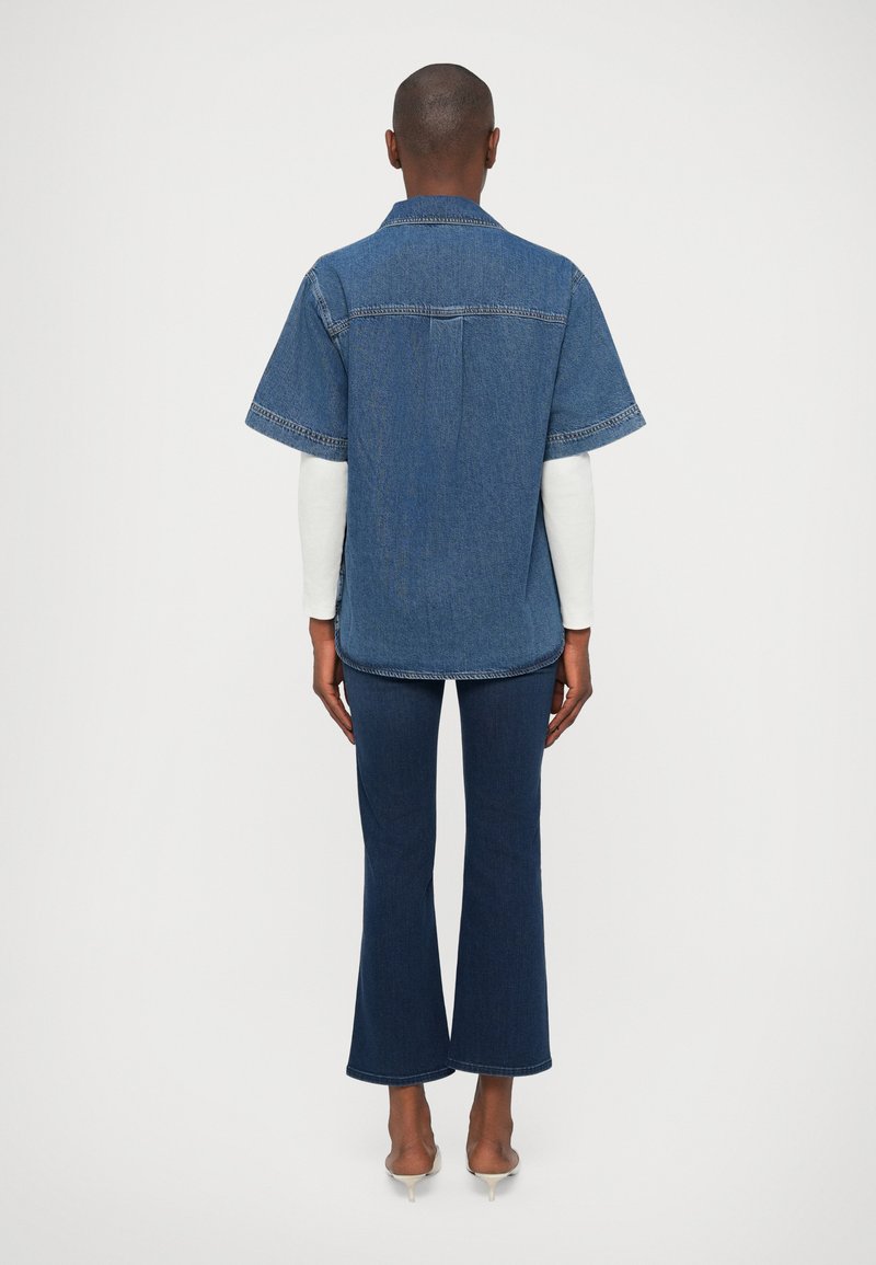 Kurze Ärmel Denimhemd, blaue Farbe, mit kontrastierenden Nähten und lässiger Passform, kombiniert mit ausgestellten Jeans in Dunkelblau.