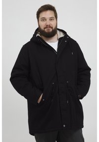 Svart parkajakke med hette, med fleeceforing, snøring i livet, frontlommer og trykknapper, vist mot en nøytral bakgrunn.