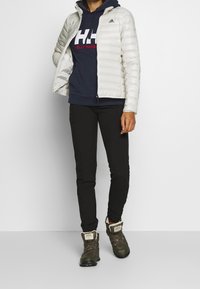 Lättvit pufferjacka med huva, marinblå hoodie under, svarta tighta byxor och gröna vandringskängor med pälsfoder.