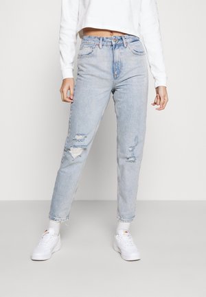 Ljusblå slitna jeans med rak benpassform som har revor och fransade nederkanter, tillsammans med vita sneakers och en kort vit sweatshirt.