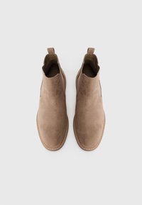 Botas de ante marrón hasta el tobillo con puntera redondeada, paneles laterales elásticos y tiradores. Presentan costuras en contraste alrededor de la suela.