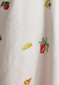 White fabric with a textured surface featuring colorful illustrations of an apple, cheese wedge, vase with leaves, and a conch shell.