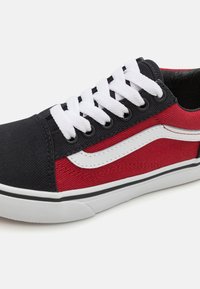 Sneakers featuring a black canvas upper, red accents, white laces, and a classic white side stripe with a black rubber sole.