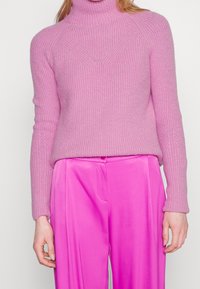 Pull à col roulé côtelé rose clair avec motif texturé et manches ajustées, associé à un pantalon satin rose vif taille haute.