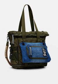 Sac fourre-tout matelassé vert olive avec poche avant en denim, fermeture éclair noire, poche latérale en mesh et patch logo. Comprend des poignées en tissu robustes.