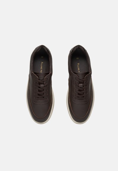 Paar donkerbruine leren sneakers met zwarte veters en witte zolen gezien van boven op een witte achtergrond.