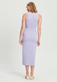 Lila mouwloze midi-jurk met een aansluitende silhouet, subtiele textuur en een centrale achterkantnaad, gecombineerd met lichte blokhakken sandalen.
