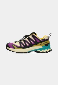 Chaussure de trail avec un dessus noir, violet et jaune, présentant un design texturé. Équipée d'un système de laçage rapide et d'une semelle robuste.