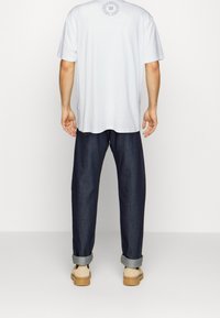 Bílý bavlněný tričko s kulatým výstřihem, v kombinaci s tmavě modrými džíny s volným střihem, s ohrnutými manžetami a béžovou obuví.