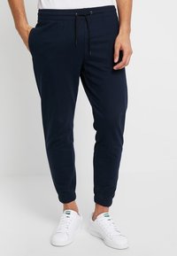 Marina joggers med elastisk midja och justerbar dragsko. Vristmanschetter. Kombination med vita sneakers. Mjukt bomullsmaterial.