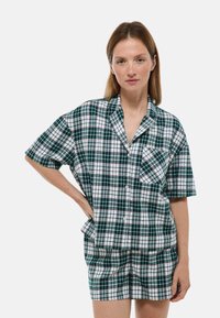 Ensemble de pyjama à manches courtes à carreaux vert, blanc et marine, comprenant une chemise à boutons, un détail de poche et un short assorti. Tissu doux.