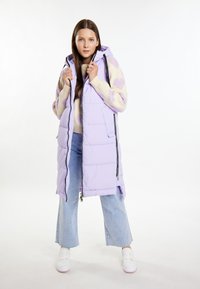 Lichtpaarse puffervest met een capuchon, voorzien van ritsen en zijzakken. Draag over een beige trui en lichtblauwe wijde jeans. Witte sneakers.