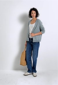 Cardigan gris clair, débardeur blanc, jeans bleus, sac beige et baskets blanches. Texture en maille lisse, coupe décontractée et silhouette relaxée.