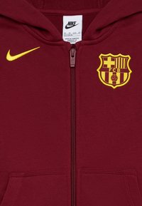 Μαροκινό φούτερ με φερμουάρ φτιαγμένο από μαλακό ύφασμα, με κίτρινο λογότυπο Nike και σήμα της Barcelona FC με κόκκινες και κίτρινες ρίγες.