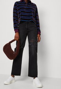 Camisa polo de manga larga a rayas marrones con cuello púrpura, combinada con unos vaqueros negros desgastados de cintura alta y zapatillas de plataforma blancas. Bolso de pelaje marrón.