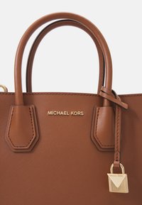 Sac à main Michael Kors en cuir marron avec double poignée et un petit charm en forme de cadenas doré suspendu à l'une des poignées.