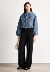 Farmerrdzseki rövidített kialakítással, lelógó vállakkal, gombos záródással, két mellzsebbel; fekete, széles szárú nadrággal és egy kis fehér táskával párosítva.