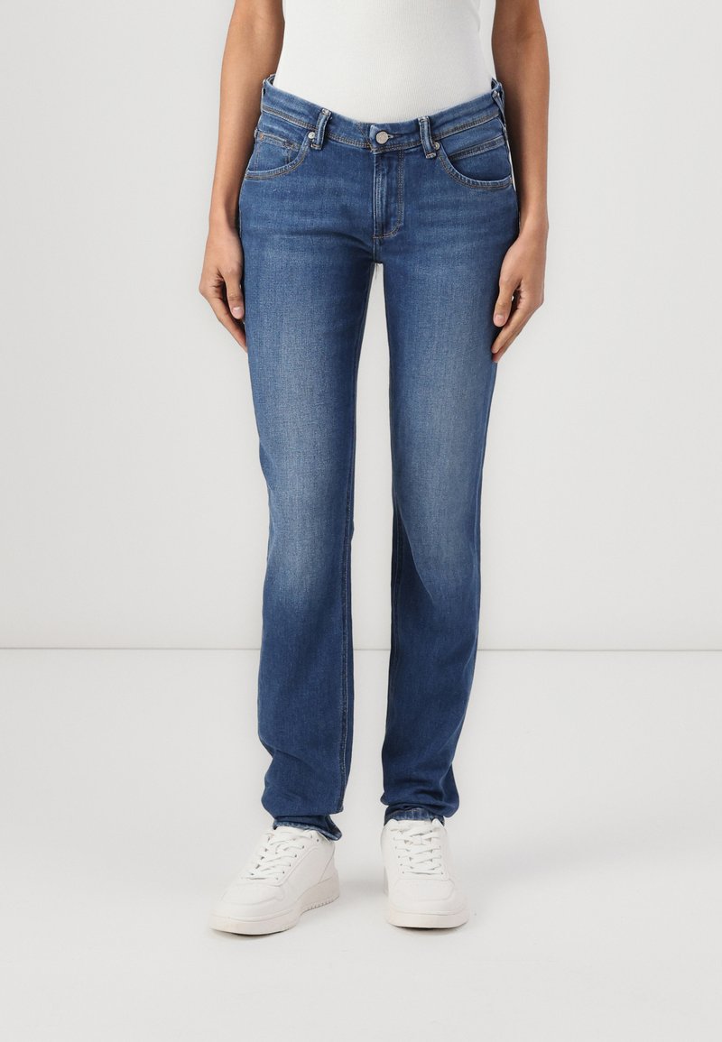 Blå denimjeans med rett ben, fem lommer, glidelås og medium vask. Kombinert med hvite sneakers.