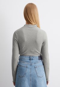 Lichtgrijs geribbeld langemouwen top met een gefronkelde kraag, gecombineerd met een blauwe denim rok met twee achterzakken en een merklabel op de taille.