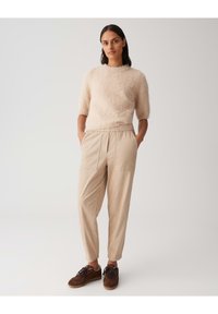 Un haut court à manches courtes en tricot flou beige clair associé à un pantalon beige ample. Des chaussures marron à lacets viennent compléter cette tenue décontractée.